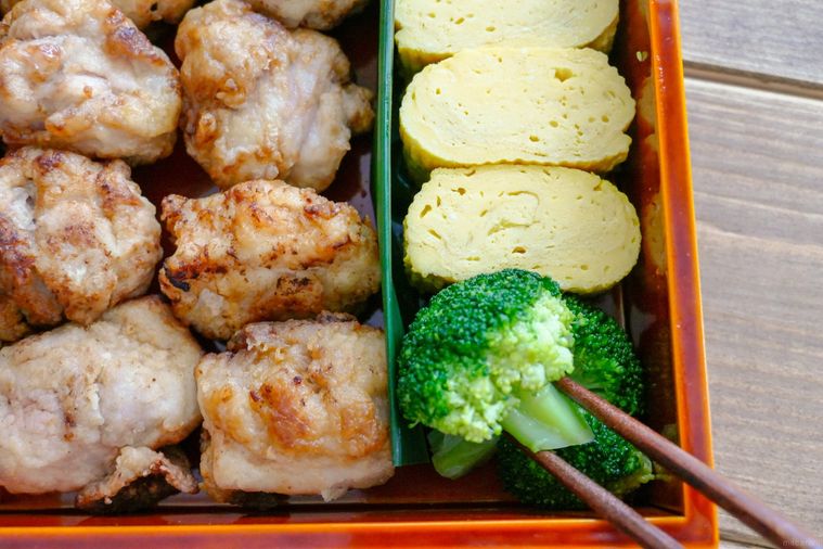 唐揚げと卵焼きが入っている弁当箱にブロッコリーを詰める様子