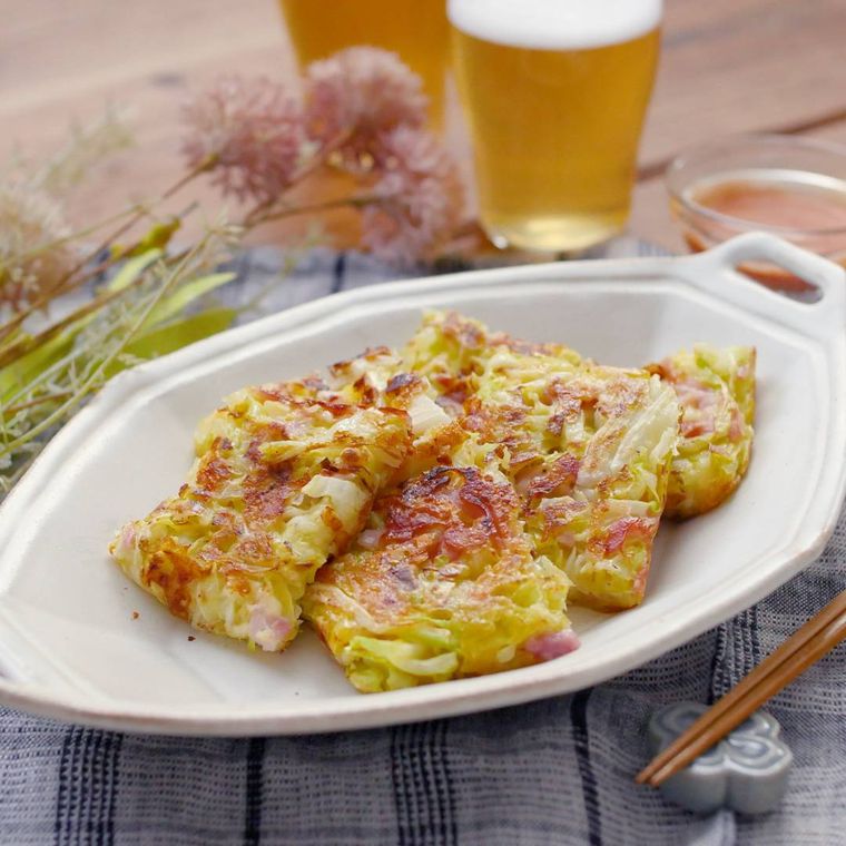 白い皿に盛りつけられたキャベツとチーズのおやきとビール、花がテーブルに置かれている