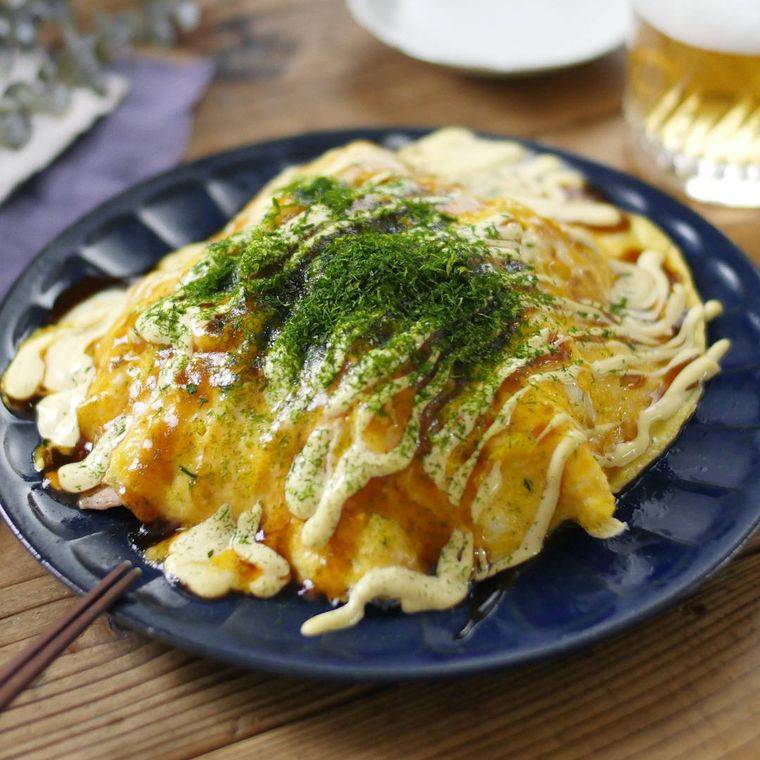 青い皿に盛りつけられた豚平焼きとビールが置かれている