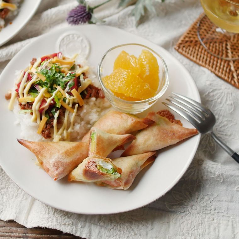 白いお皿に盛り付けられたアボカドと明太子の春巻きとタコライス、カットされたフルーツ