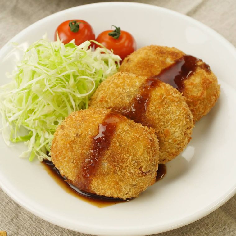 白い皿に盛りつけられたポテトコロッケとつけ合わせのキャベツ