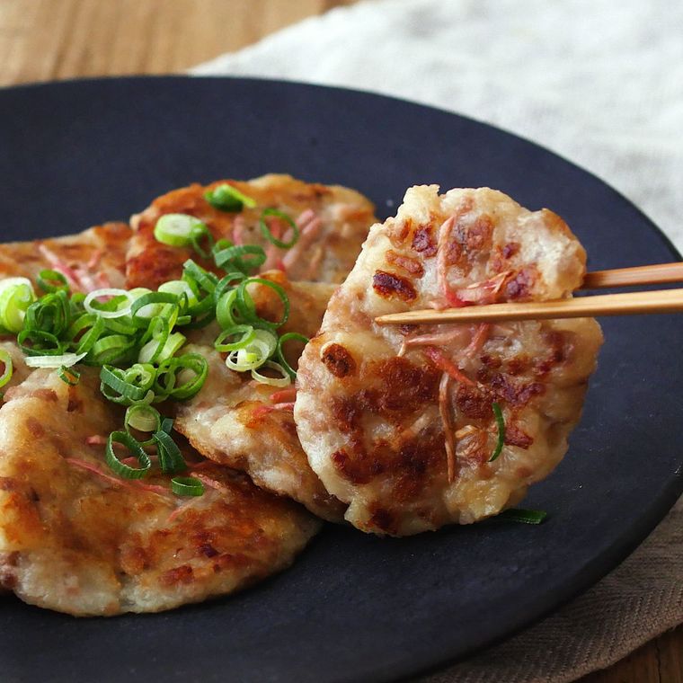 皿に盛りつけられたちくわと豚肉の長芋焼きを箸でつまんでいる様子と、下に敷かれたグレーのテーブルクロス