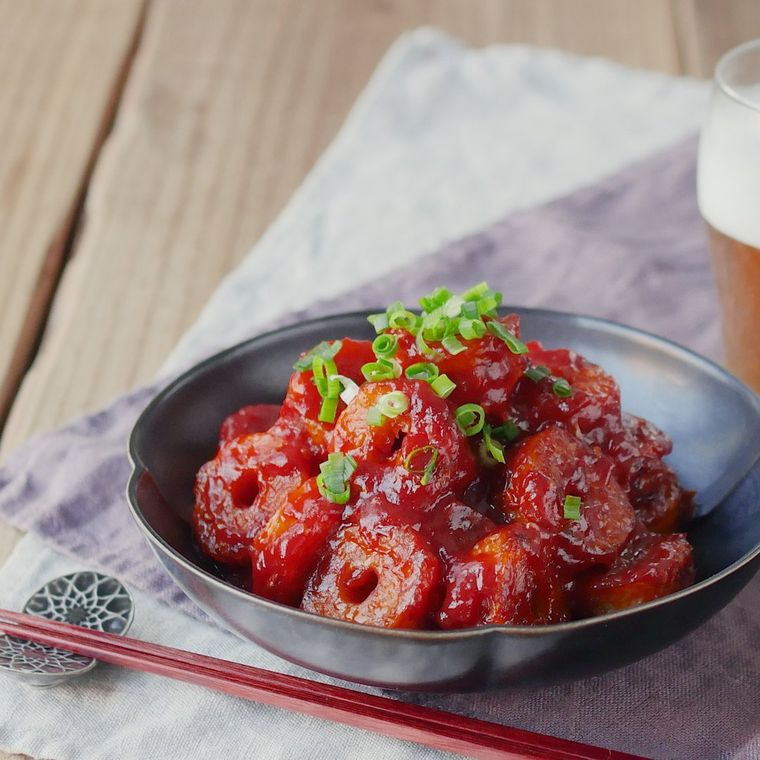 黒い深皿に盛りつけられているちくわのチリソース炒めと青ねぎに、箸置きに置かれた箸とビール入りのグラスが添えられている