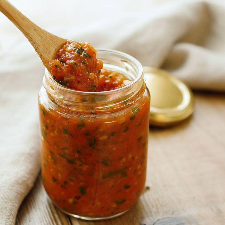 ガラス瓶に入ったトマトバジルソースを竹製のスプーンですくう様子