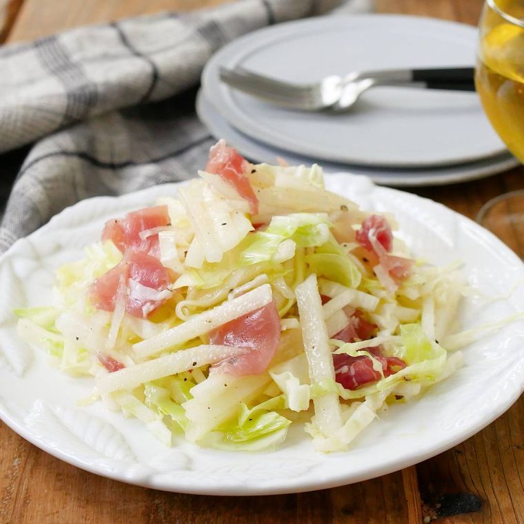 白い皿に盛りつけられている生ハムと梨入りのキャベツサラダ