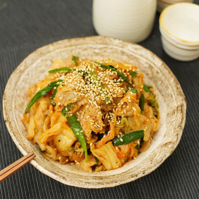 お皿に盛られた豚とキムチの野菜炒めに箸を添えている