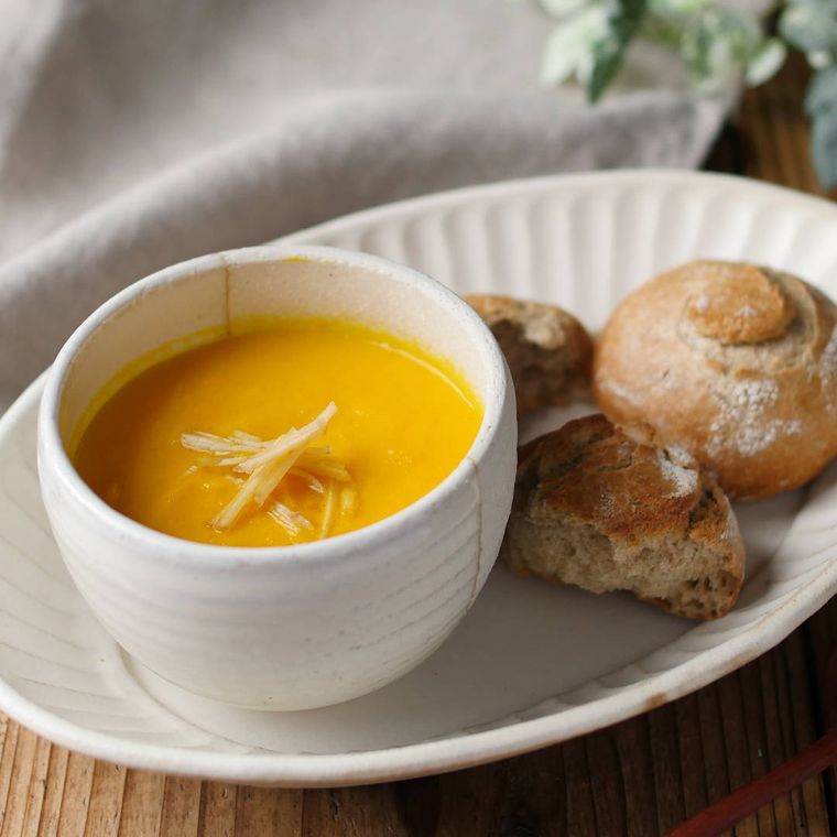 白いスープ皿に盛りつけられたにんじんコンソメ豆乳スープ