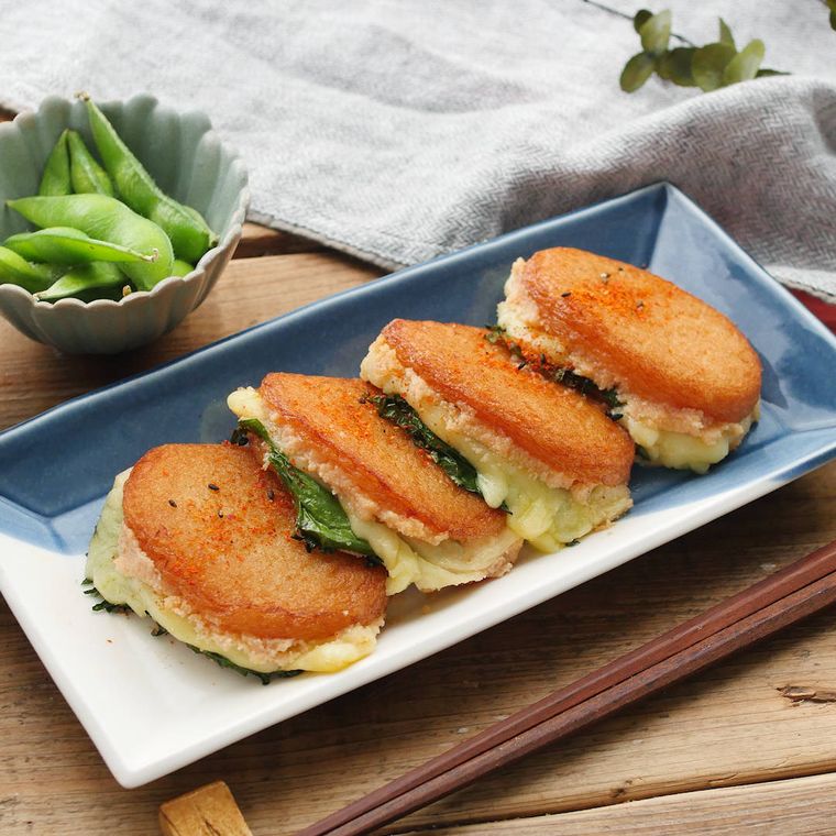 青と白の角皿に並べられた4つのさつまあげの明太マヨはさみ焼きと、白い小鉢に盛られたえだまめ、箸置きに置かれた箸