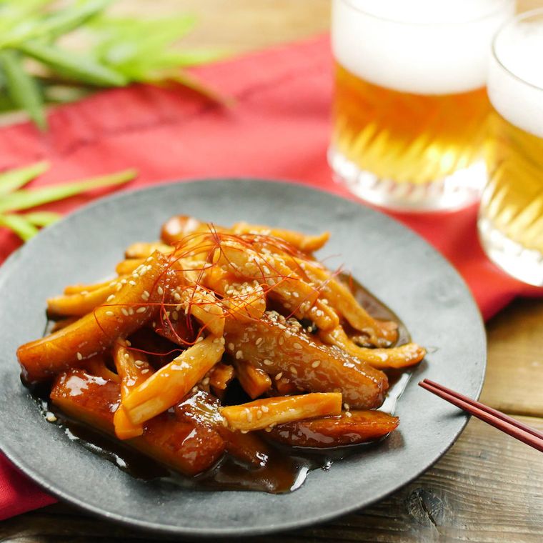 黒いお皿に盛り付けられたエリンギとさつまあげのトッポギ風に、箸とグラス入りのビール2杯が添えられている