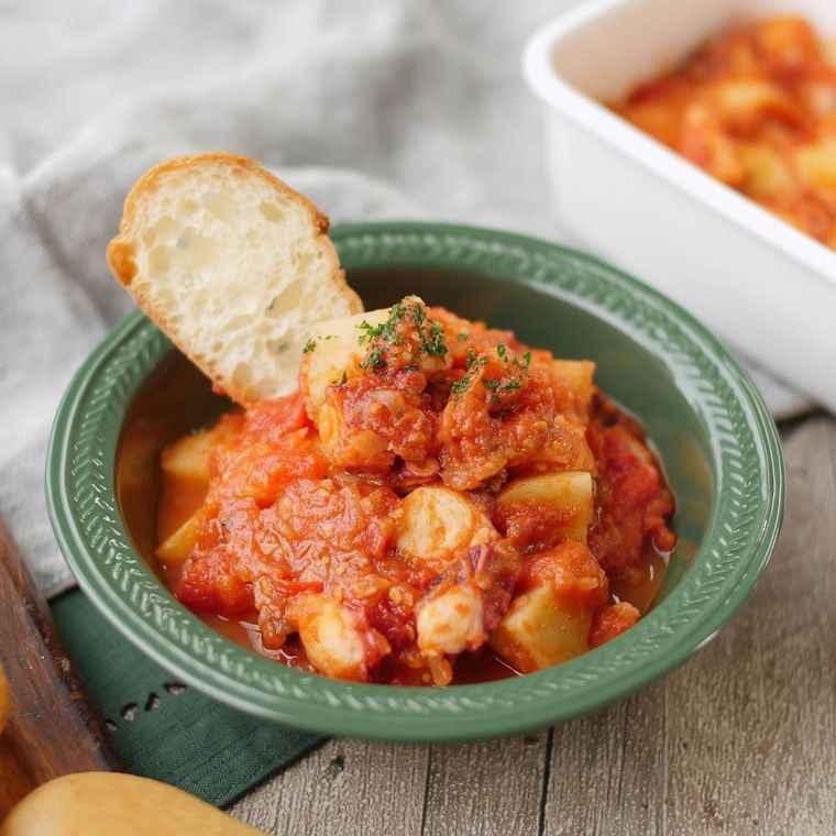 緑色の皿に盛りバゲットを添えた、たことじゃがいもの煮込み