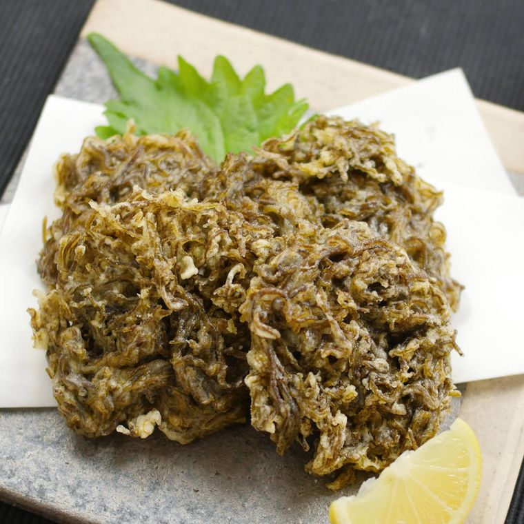 白い敷き紙の上に盛りつけられた、もずくの天ぷらとカットレモン