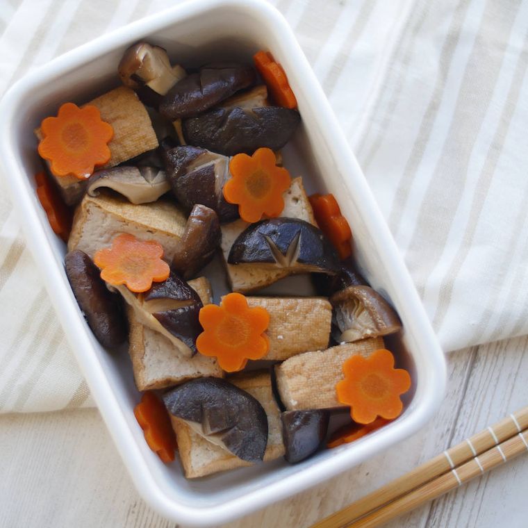 白い保存容器に入っているしいたけと厚揚げ、梅形にんじんの旨煮
