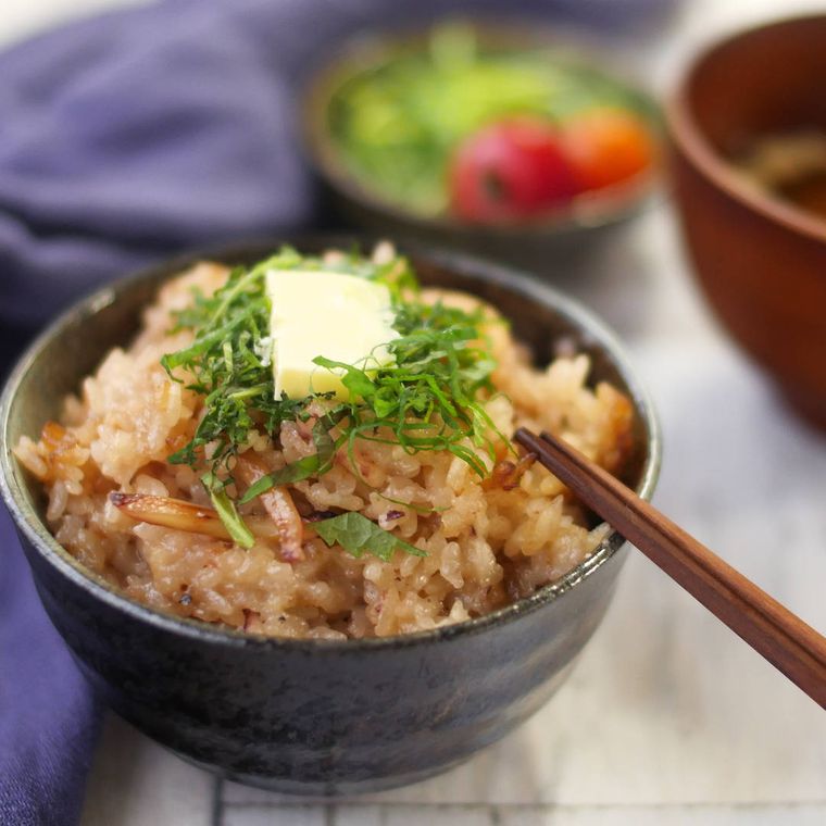 黒い茶碗に盛りつけられたいかと切り餅入りの炊き込みごはん