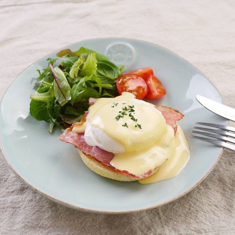 淡色の皿に盛りつけられたエッグベネディクトとつけ合わせの野菜
