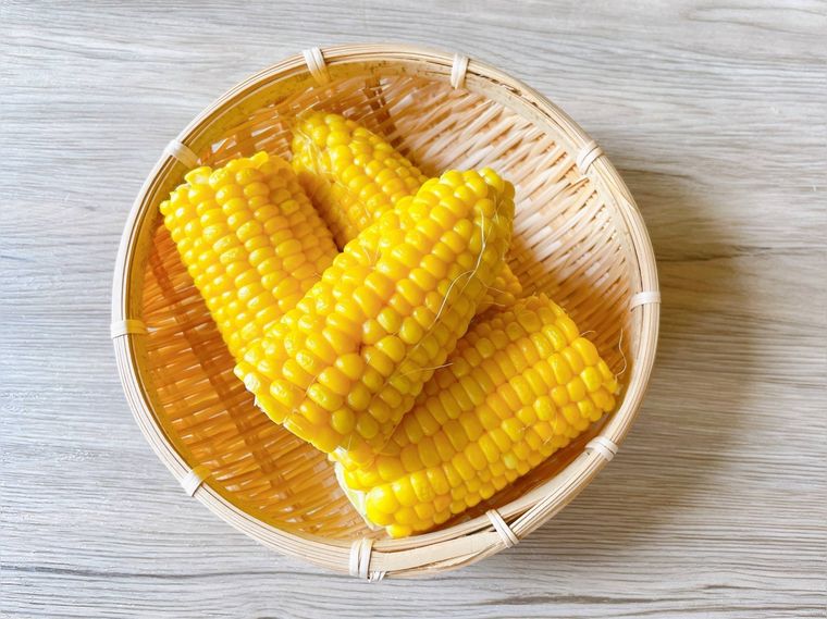 ざるにのった、皮をむいている蒸しとうもろこし