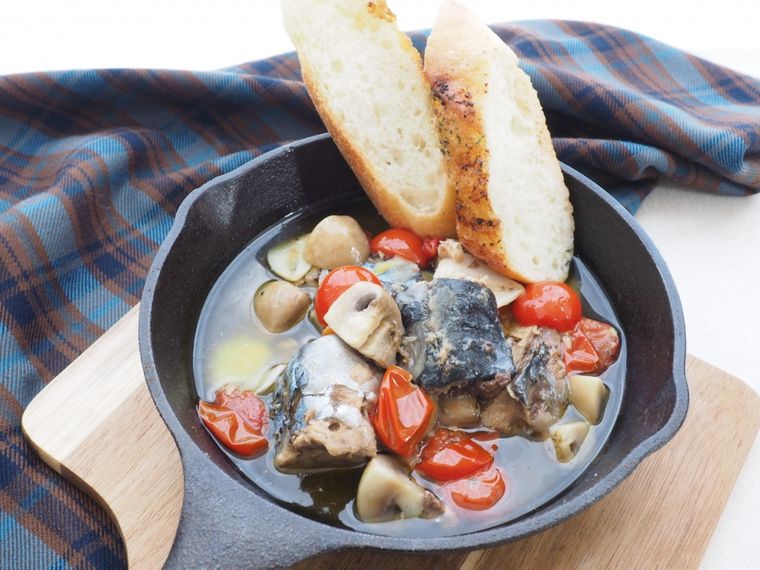 スキレットに入っているさば缶アヒージョにバゲットをつけている様子