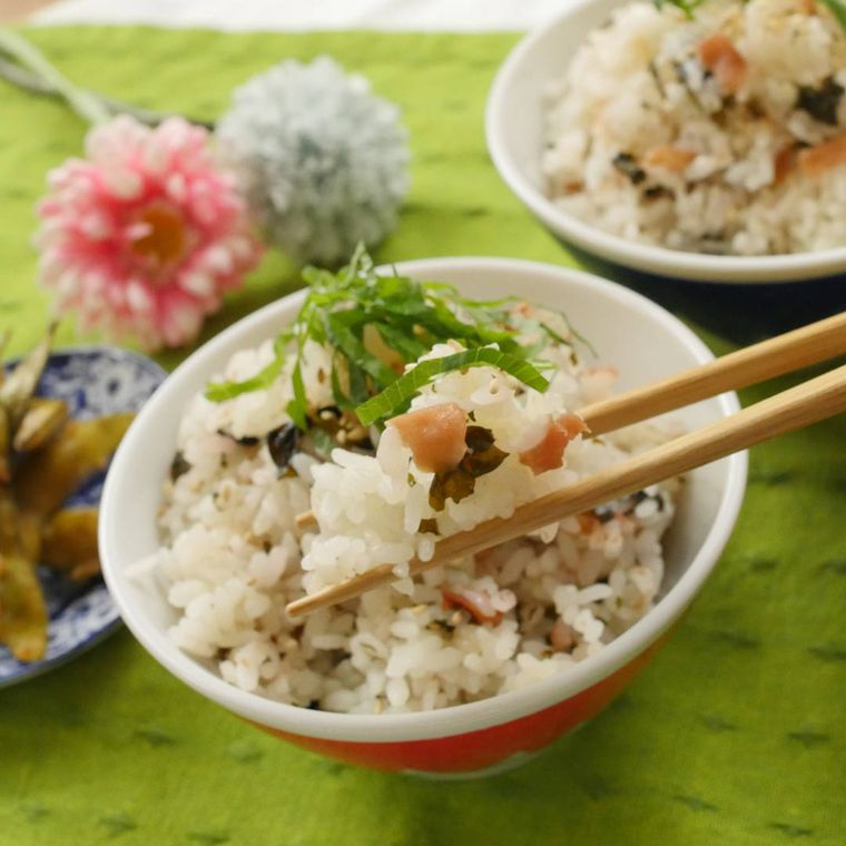 茶碗に盛られた梅干しとわかめの炊き込みご飯を箸で挟んでいる様子