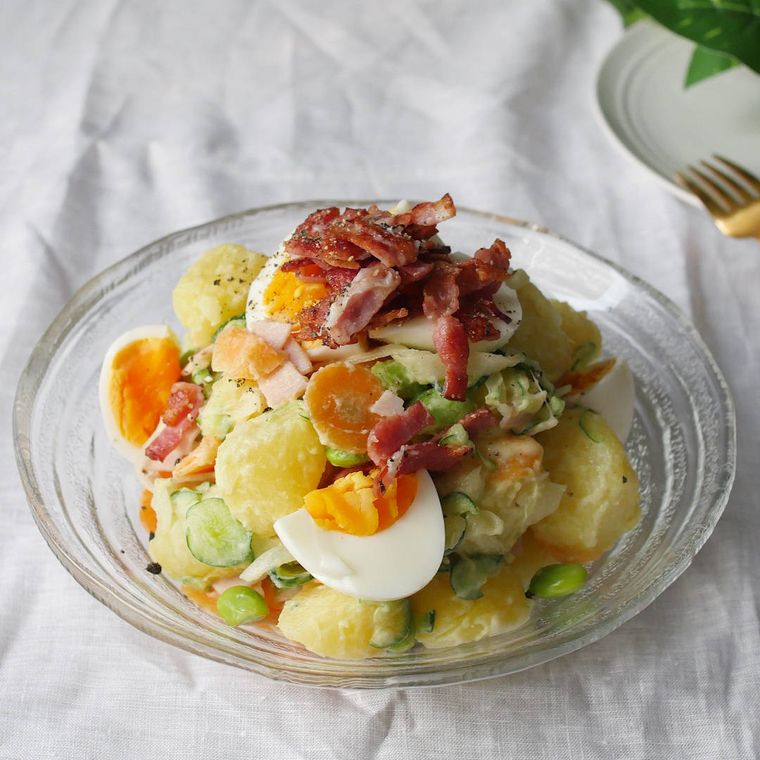 ガラス皿に盛りつけられた、ベーコンやゆで卵入りのポテトサラダ