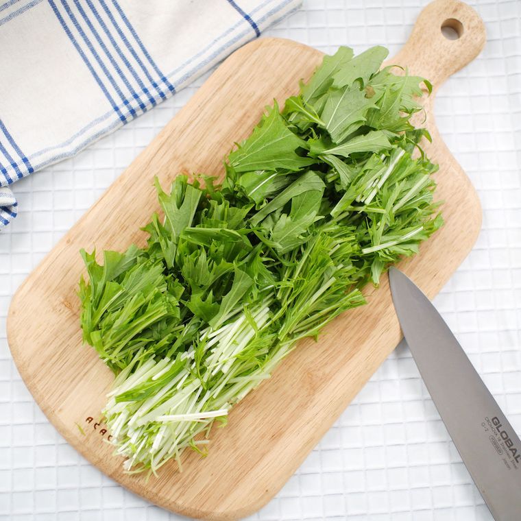 木製のカッティングボードの上にある、ざく切りにした水菜