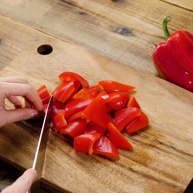 丸ごとの赤パプリカとまな板の上で乱切りされているパプリカ