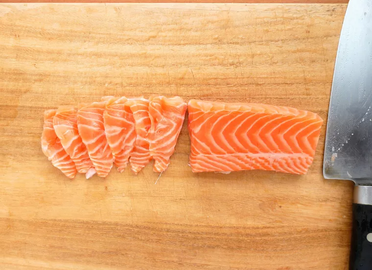 まな板の上でサーモンの柵を包丁でそぎ切りしている様子