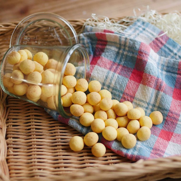 チェック柄のふきんを置いた四角いかごの上に、ガラスのカップを倒して盛られたにんじんボーロ