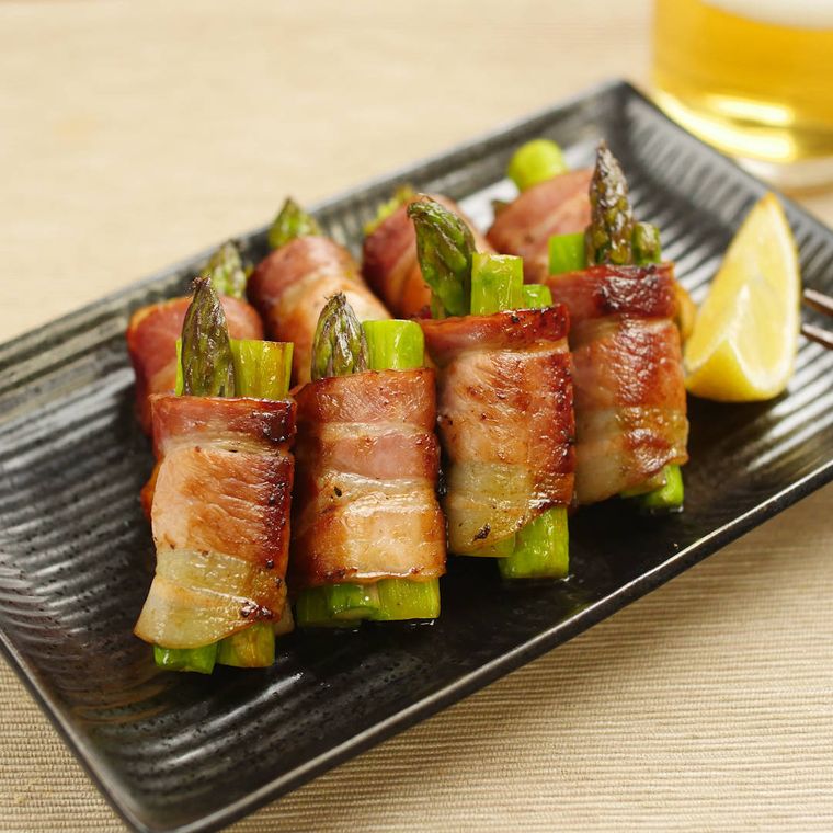 こげ茶色の長皿に盛りつけられたアスパラガスのベーコン巻き焼き