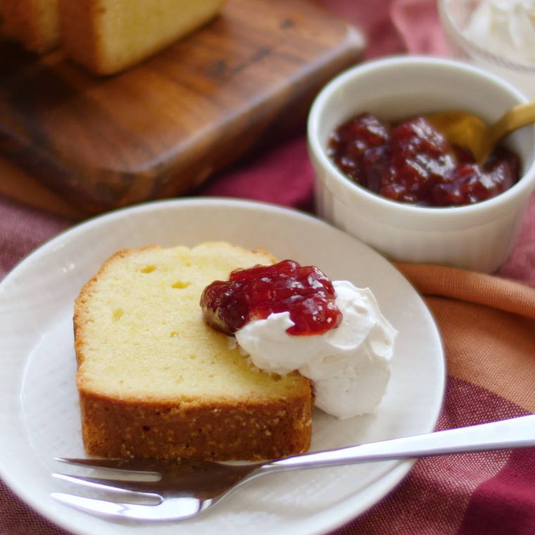 白い皿に盛り付けたベーキングパウダーなしパウンドケーキにジャムと生クリームを添えて