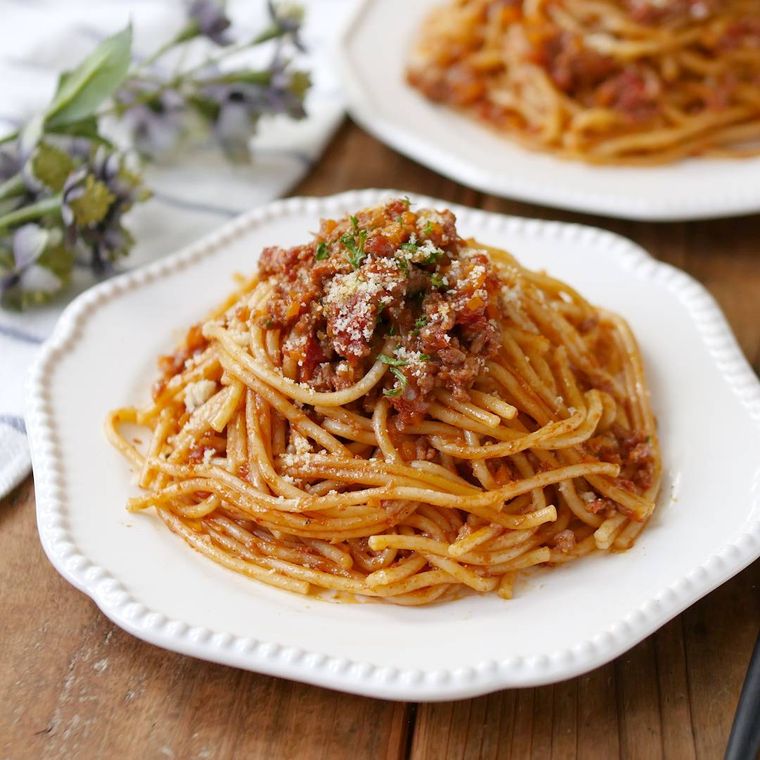 縁取りのある白い皿に盛りつけられたラグーソーススパゲッティ
