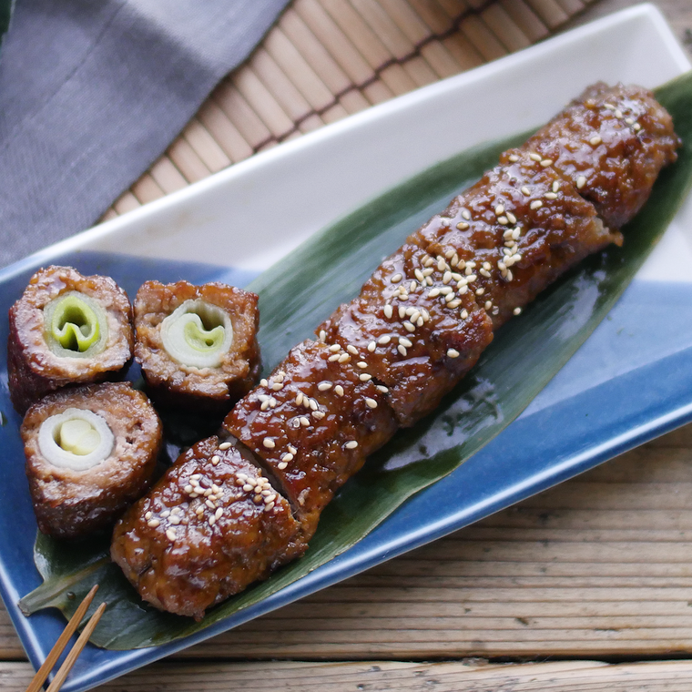 ツートンカラーの長皿に盛りつけられた白ねぎの甘辛つくね巻き