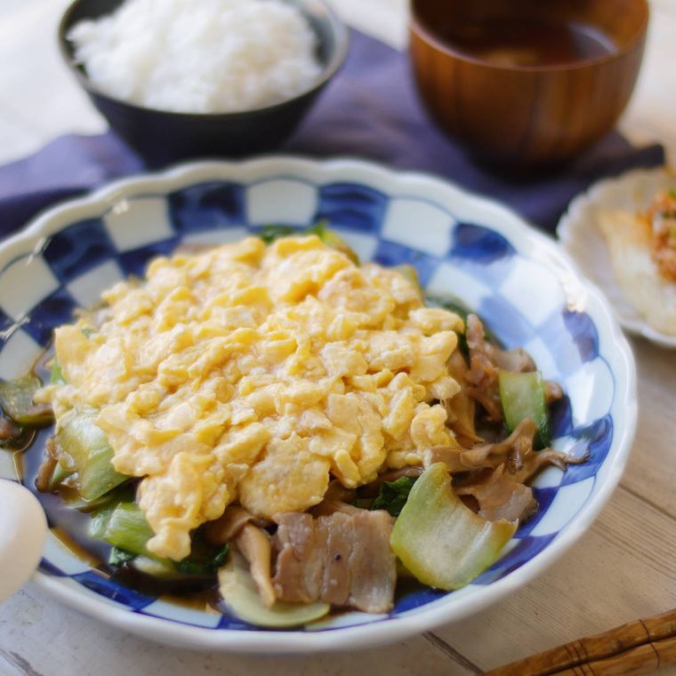 丸い皿に卵とチンゲン菜のオイスター炒めが盛られ、ごはんやみそ汁が添えられている様子