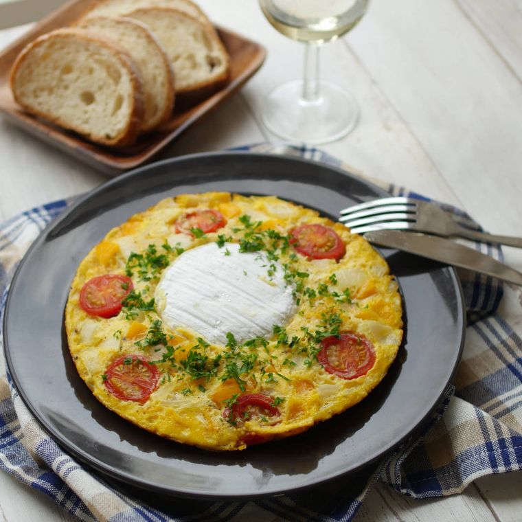 丸皿に盛り付けられた、まるごとのカマンベールチーズが入った、ミニトマトやにんじん入りのオムレツ