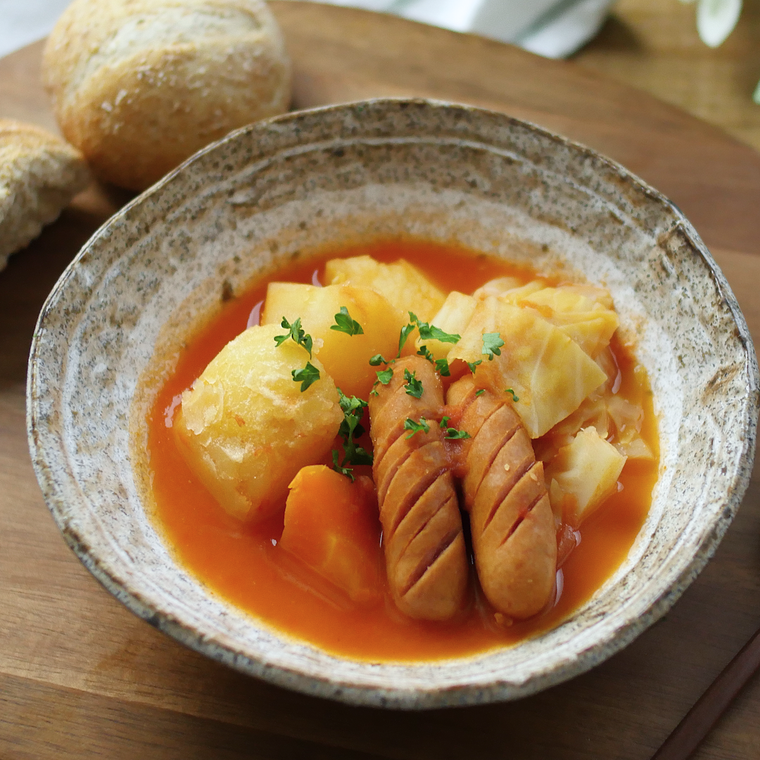 陶器に盛り付けたソーセージと野菜のトマトスープ