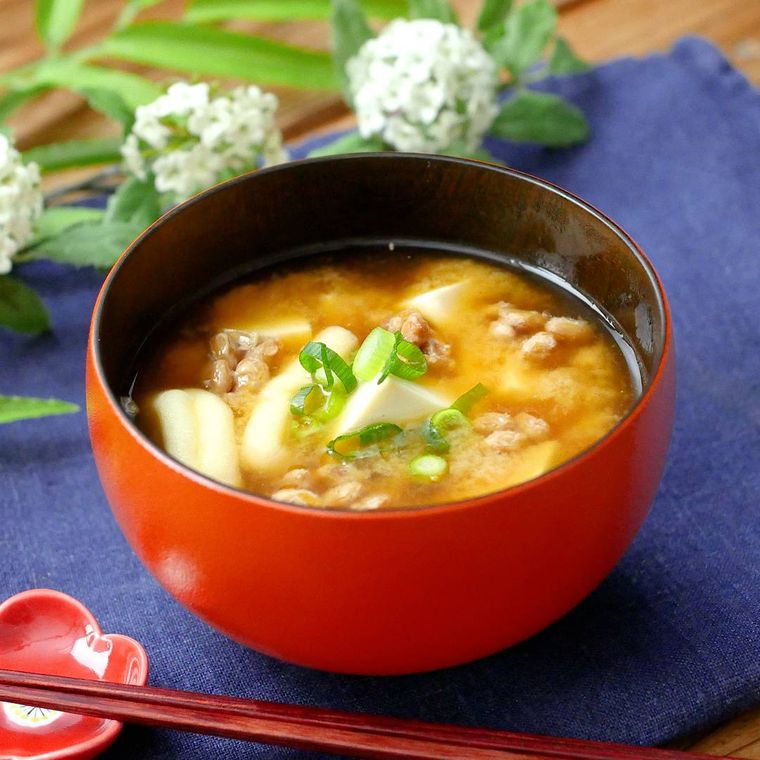 赤い汁椀に盛られている納豆と油揚げと絹豆腐の味噌汁