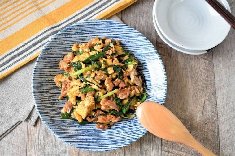 青い器に盛られた豚肉ニラ玉、サービングスプーン、取り皿がテーブルの上に並んでいる