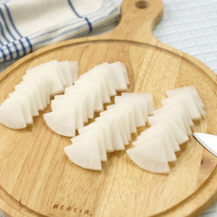 丸いカッティングボードの上でいちょう切りにされた大根