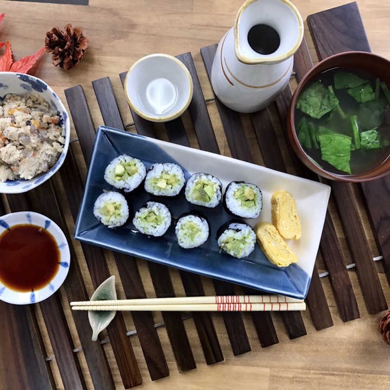 青い皿に盛られたアボカドとたくあんの海苔巻き