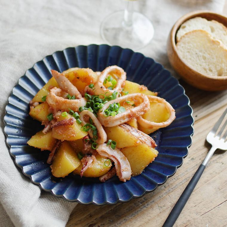 青い皿に盛られたいかとじゃがいもの明太バターしょうゆ炒め
