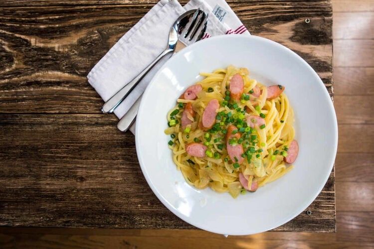 白い丸皿に盛り付けられたウインナーと玉ねぎの醤油バターパスタ