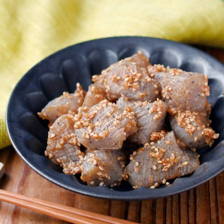 黒い器に盛られたこんにゃくのごまみそ炒めに、箸置きに置かれた箸・黄色いテーブルクロスが添えられている