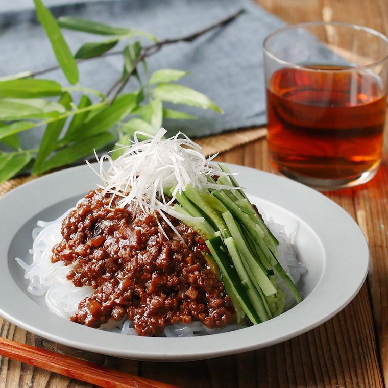 白い平皿に盛り付けられた糸こんにゃくのジャージャー麺と、コップに入った麦茶