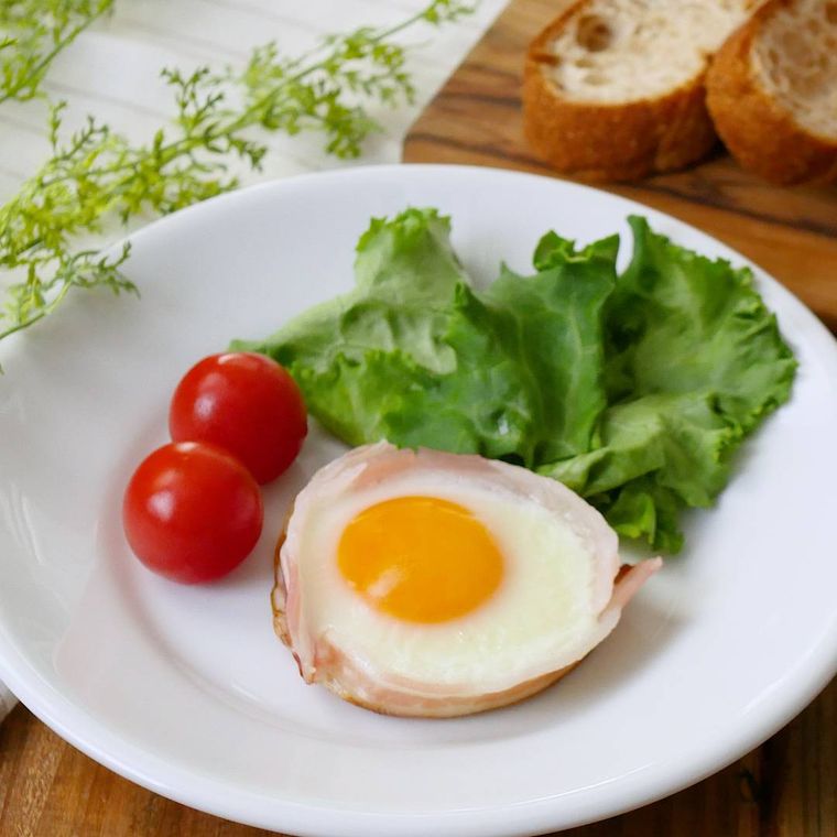 白い皿に盛りつけられたまんまるベーコンエッグにミニトマトとレタスが添えられている