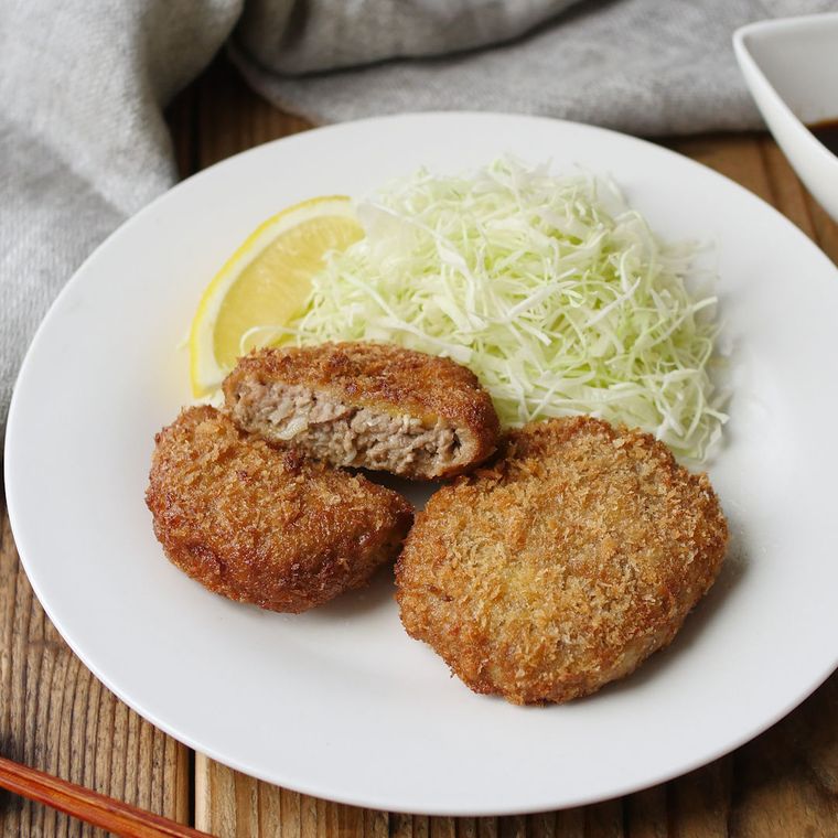 白い皿に盛りつけられたメンチカツにせん切りキャベツとレモンが添えられている