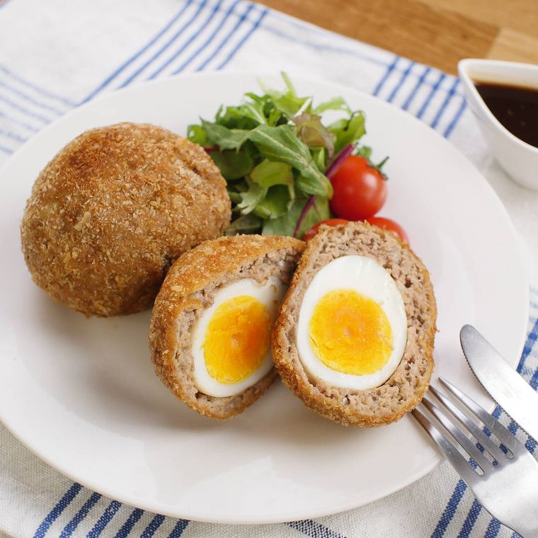 皿に盛りつけられたスコッチエッグにベビーリーフとミニトマトが添えられている