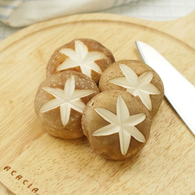 丸いカッティングボードの上で軸を落とし飾り切りされたしいたけ