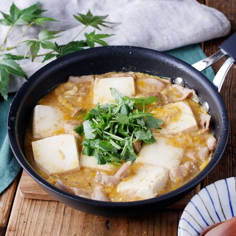 カッティングボードの上の、フライパンに入った豚バラ肉と絹豆腐の卵とじ