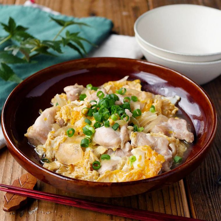 飴色の皿に盛り付けた鶏もも肉と玉ねぎの卵とじと、ふたつの白い取り皿