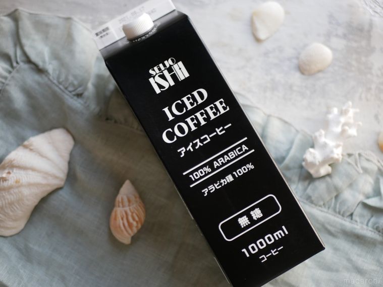 布の上に白い貝殻と成城石井のアイスコーヒー無糖が置いてある