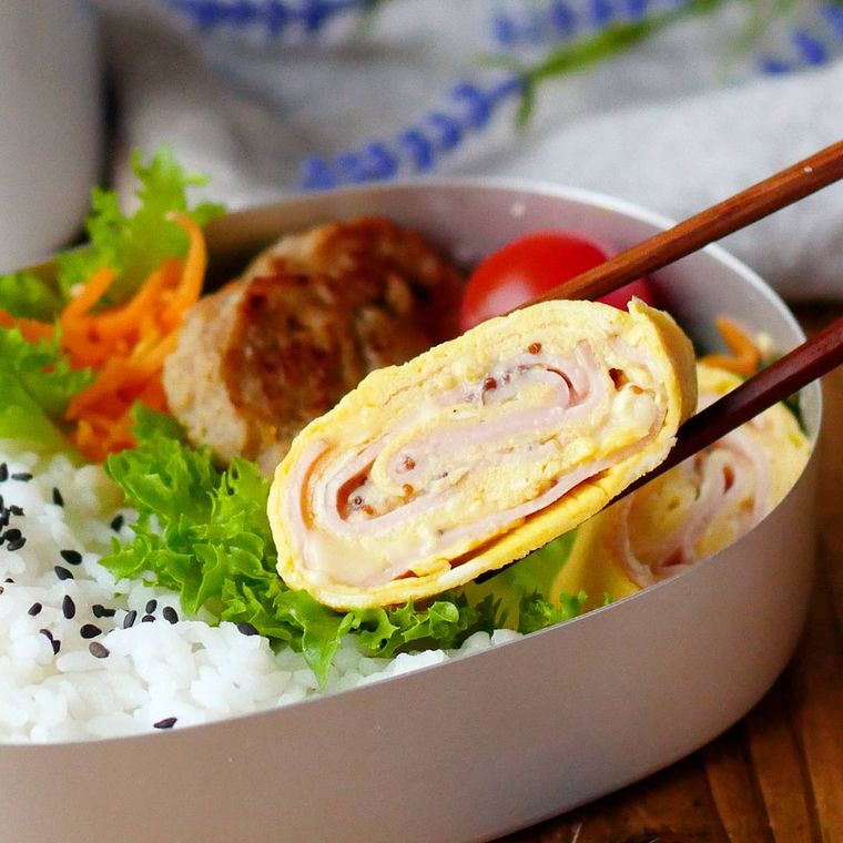 弁当箱に入っているハムとチーズの卵焼きを、箸でつまんだ様子
