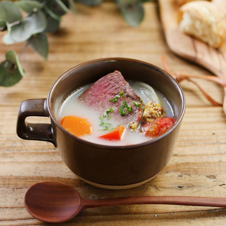 片手の茶色のマグカップに盛りつけられた牛肉のメープル煮込みスープ